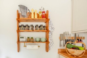 A kitchen with wooden shelves holding spices, a digital clock, and a basket of vegetables. - 2 Bed in Evercreech (oc-t40223) (Evercreech)
