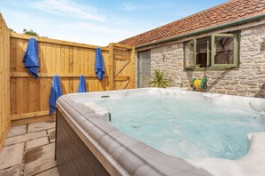 A hot tub in a backyard with a wooden fence and a stone building.