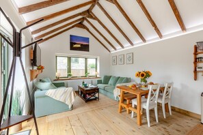 A cozy living room with a wooden ceiling, a sofa, a dining table with chairs, and a window with a view of the outside.