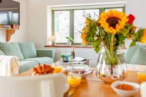A cozy living room with a sofa, a coffee table with breakfast items, and a window with a view of a building. - 2 Bed in Evercreech (oc-t40223) (Evercreech)