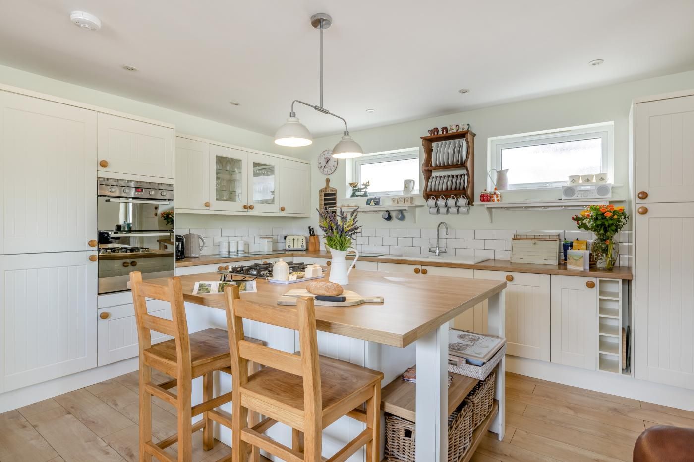 A modern kitchen with white cabinetry, a wooden dining table, and a pendant light.
