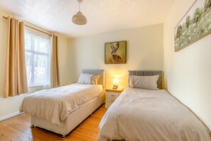 Quarto com duas camas, mesa de cabeceira com abajur, janela com cortinas e um quadro na parede.