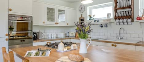 A modern kitchen with white cabinetry, a central island, a gas stove, and a wooden dining table.