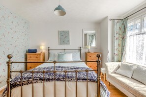 A bedroom with a bed, bedside tables, a hanging light fixture, a window with curtains, and a wall-mounted mirror. - 3 Bed in Braunton (oc-m45420) (Braunton)