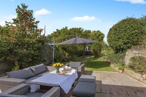 An outdoor patio with wicker furniture, a table with a white tablecloth, and a large umbrella. - 3 Bed in Braunton (oc-m45420) (Braunton)