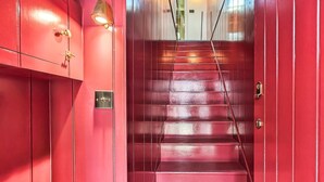 A red staircase with a metal railing, a wall-mounted light fixture, and a door with a lock. - 1 Bed in Swanage (oc-s45891) (Swanage)