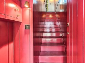 Eine rote Treppe mit Metallgeländer, einer Wandleuchte und einer Tür mit Schloss.