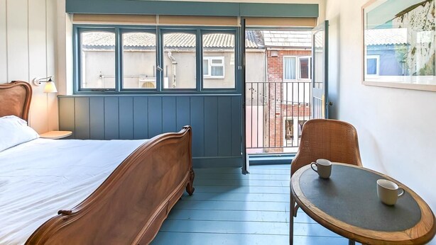 A bedroom with a bed, a table with two cups, a hanging lamp, and a view of a balcony with a railing. - 1 Bed in Swanage (oc-s45891) (Swanage)