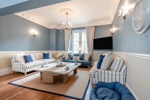 A living room with two sofas, a coffee table, and a TV mounted on the wall. - 9 Bed in Tenby (oc-h45564) (Tenby)