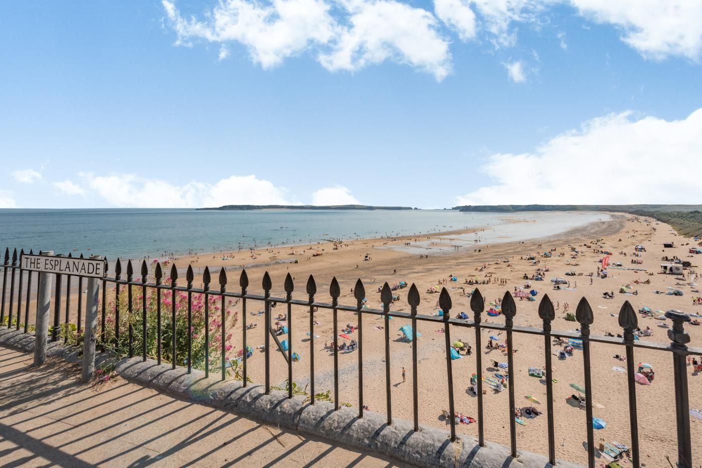 Een strand met een bord waarop 'THE ESPLANADE' staat en een stenen balustrade op de voorgrond.
