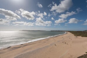 A beach with a clear sky and calm sea, featuring a sandy shore and distant land. - 9 Bed in Tenby (oc-h45564) (Tenby)