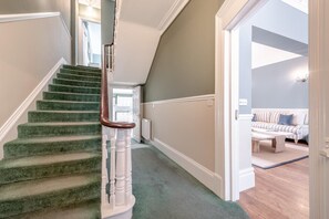 A staircase with green carpeted steps and white balusters, leading to a room with a striped sofa and a wooden coffee table. - 9 Bed in Tenby (oc-h45564) (Tenby)