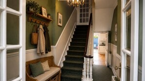 A hallway with a staircase, a bench, and a coat rack with hanging items. - 9 Bed in Tenby (oc-h45564) (Tenby)