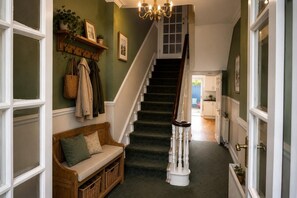 A hallway with a staircase, a bench, and a coat rack with hanging items. - 9 Bed in Tenby (oc-h45564) (Tenby)