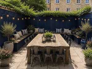 An outdoor dining area with a wooden table and chairs, surrounded by planters and a blue fence with climbing plants. - 9 Bed in Tenby (oc-h45564) (Tenby)