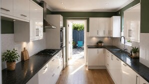 A modern kitchen with white cabinets, a black countertop, and a wooden floor. - 9 Bed in Tenby (oc-h45564) (Tenby)