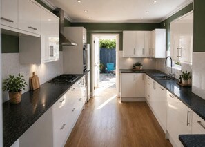A modern kitchen with white cabinets, a black countertop, and a wooden floor. - 9 Bed in Tenby (oc-h45564) (Tenby)