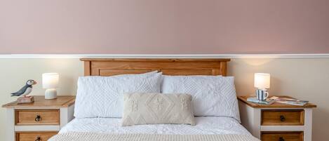 A bed with a wooden headboard, two bedside tables with lamps, and a decorative bird on one table.