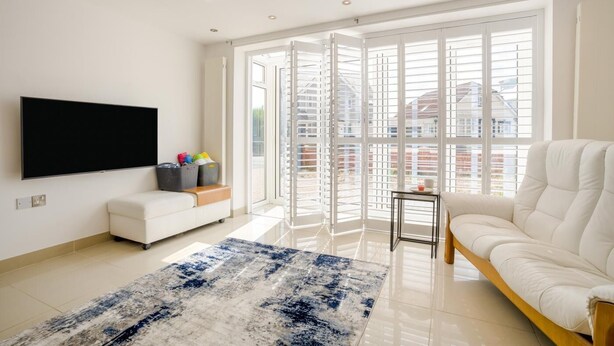 A modern living room with a flat-screen TV, a white sofa, a blue and white rug, and a sliding glass door leading to a balcony. - 2 Bed in Bournemouth (oc-f45847) (Bournemouth)