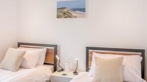 A hotel room with two beds, a nightstand, a lamp, and a wall-mounted picture of a beach. - 2 Bed in Bournemouth (oc-f45847) (Bournemouth)