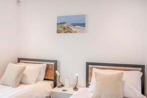 Ein Hotelzimmer mit zwei Betten, einem Nachttisch, einer Lampe und einem an der Wand hängenden Bild von einem Strand.