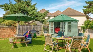 A backyard with a wooden table and chairs, a barbecue grill, and a small shed. - 2 Bed in Bournemouth (oc-f45847) (Bournemouth)