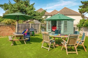 Ein Garten mit Holztisch und -stühlen, einem Grill und einem kleinen Gartenhaus.