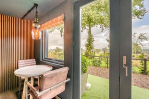 A room with a dining table and chairs, a window with a view of a garden, and a door leading outside.