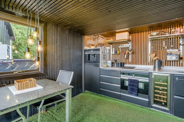 A modern kitchen with a built-in oven, a dining area with a table and chairs, and a window with hanging light bulbs.
