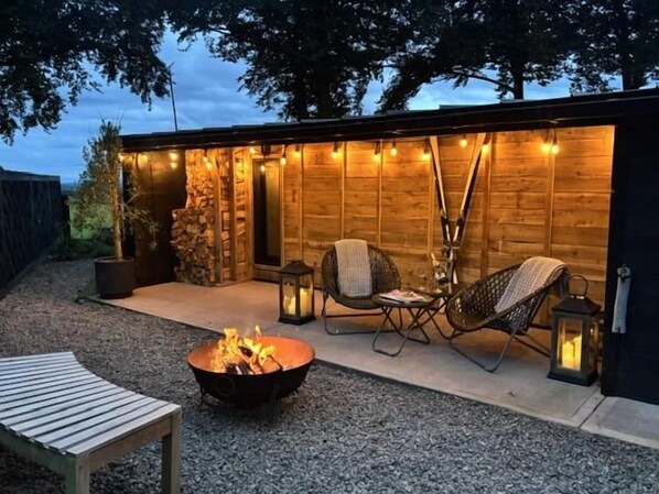 A cozy outdoor seating area with a fire pit, two wicker chairs, and a wooden table.