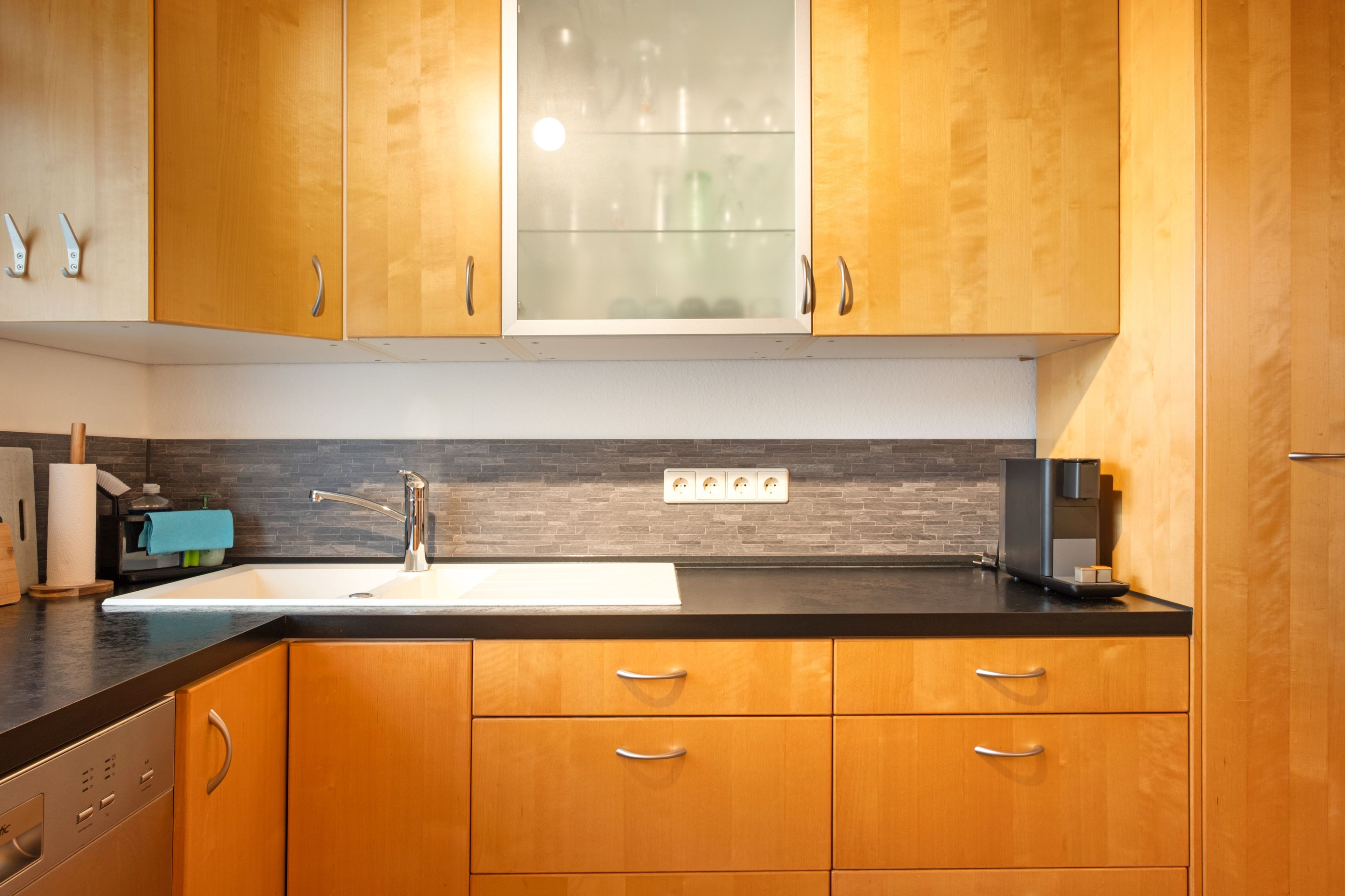 A kitchen with wooden cabinets, a stainless steel sink, and a black countertop.