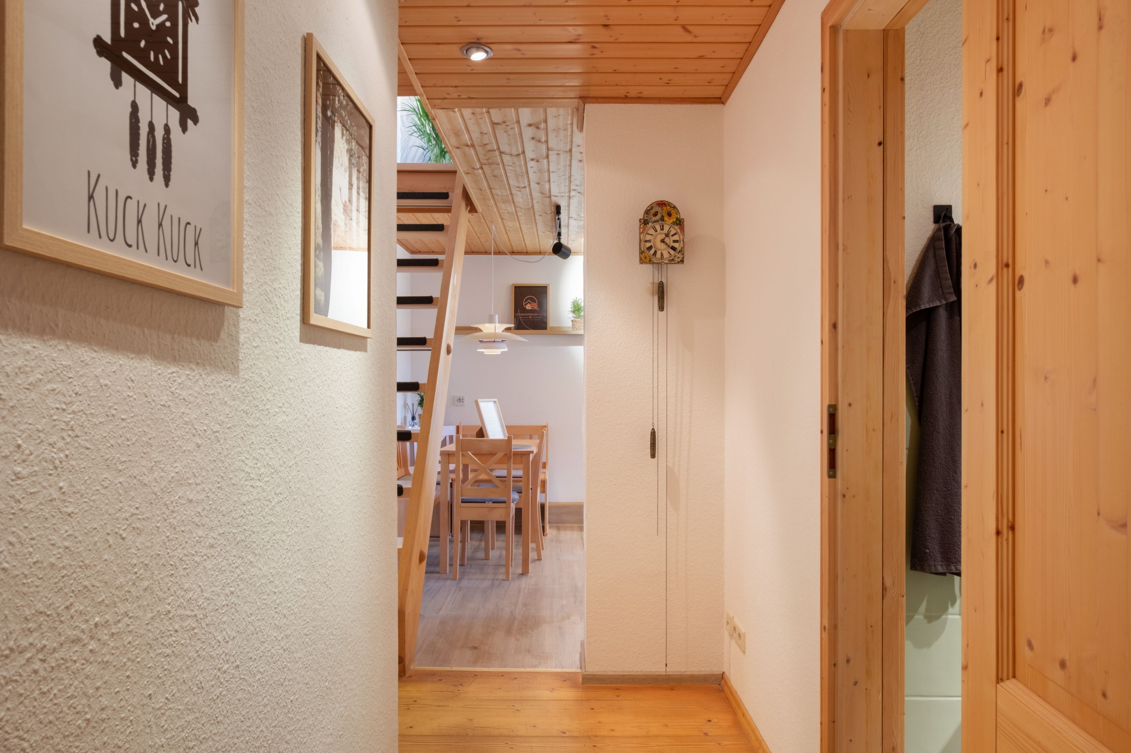 Ein Flur mit Holzboden, einer Uhr an der Wand und einem gerahmten Bild mit Text.