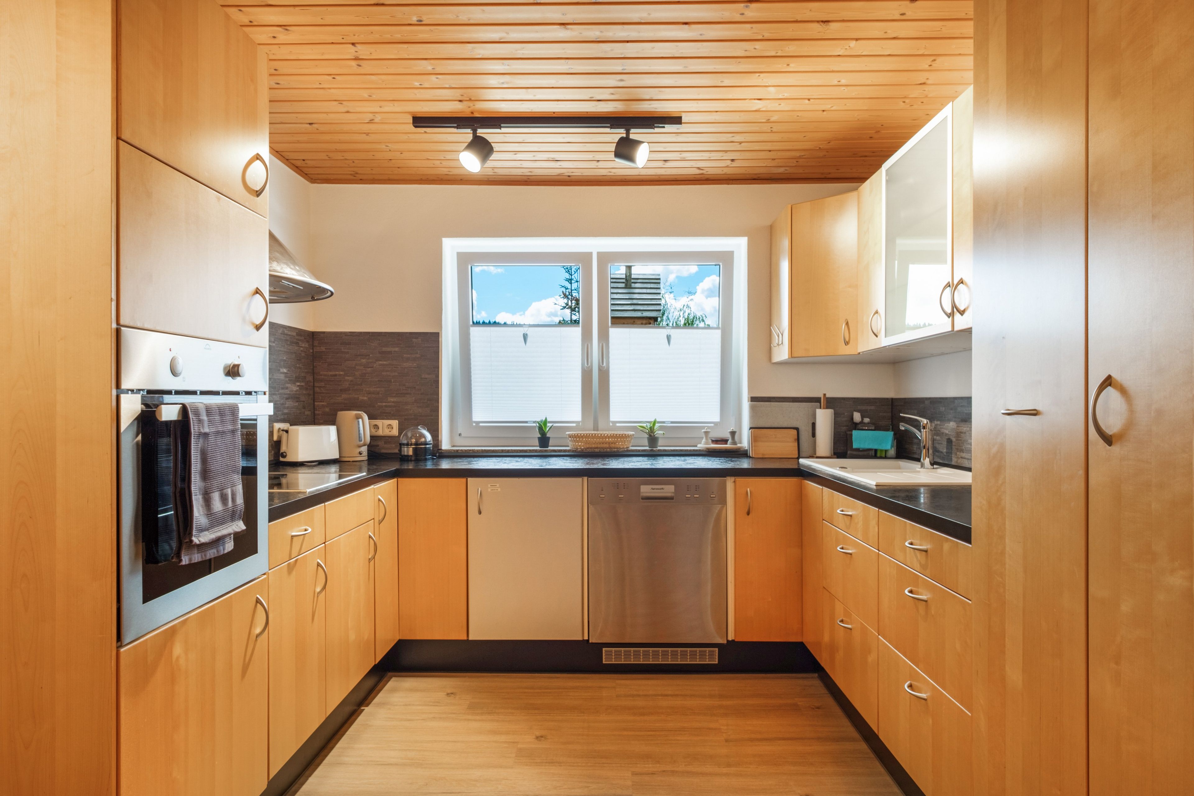 A modern kitchen with wooden cabinets, a black countertop, and a window with a view of the outdoors.