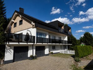A two-story house with a garage, a balcony, and a well-maintained lawn. - Schwarzwaldmarie Apartment Schönwald: Balcony, Stunning View, Wi-Fi (Schönwald im Schwarzwald)