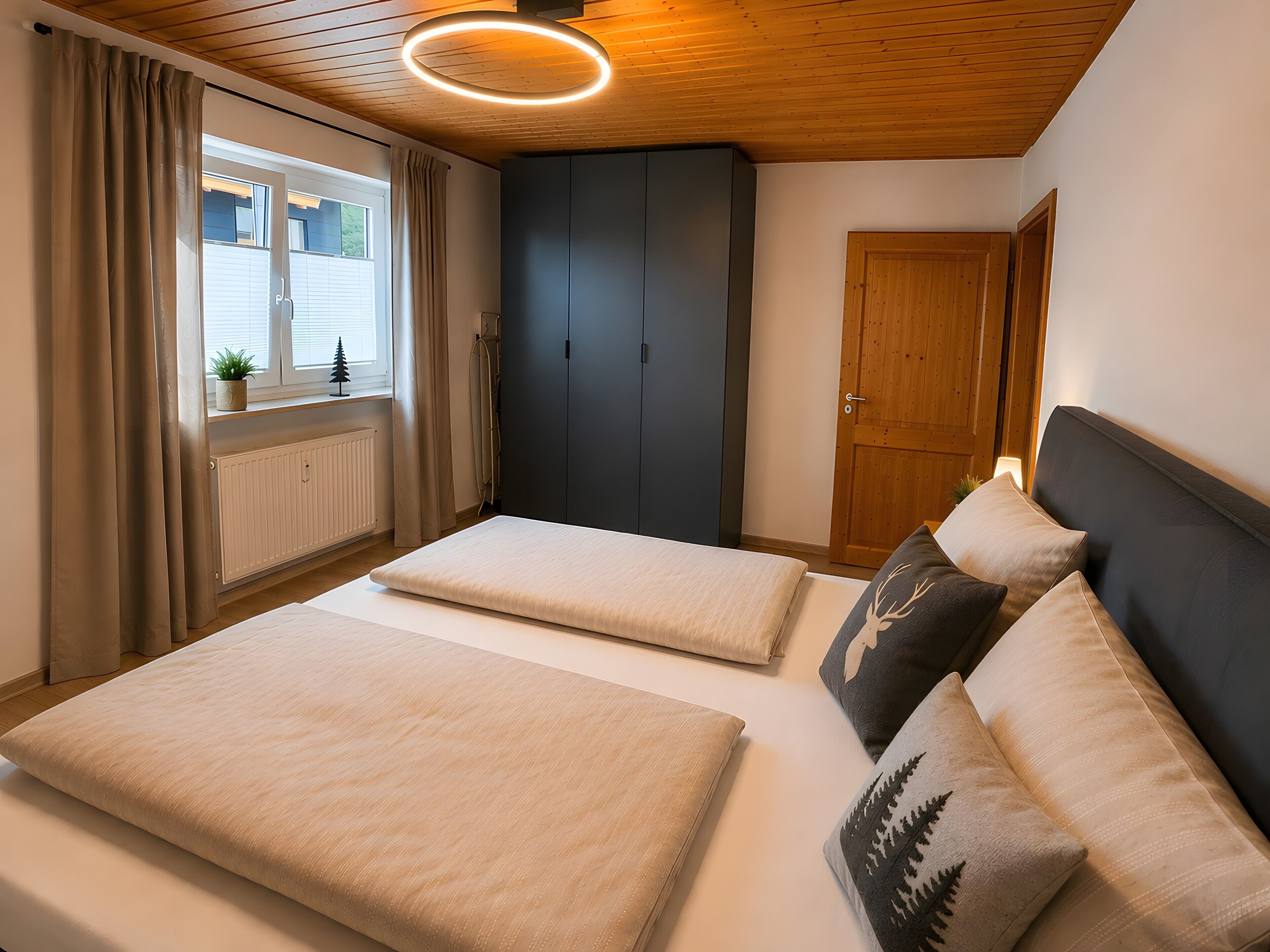 A bedroom with a bed, a wardrobe, a window with curtains, and a door.