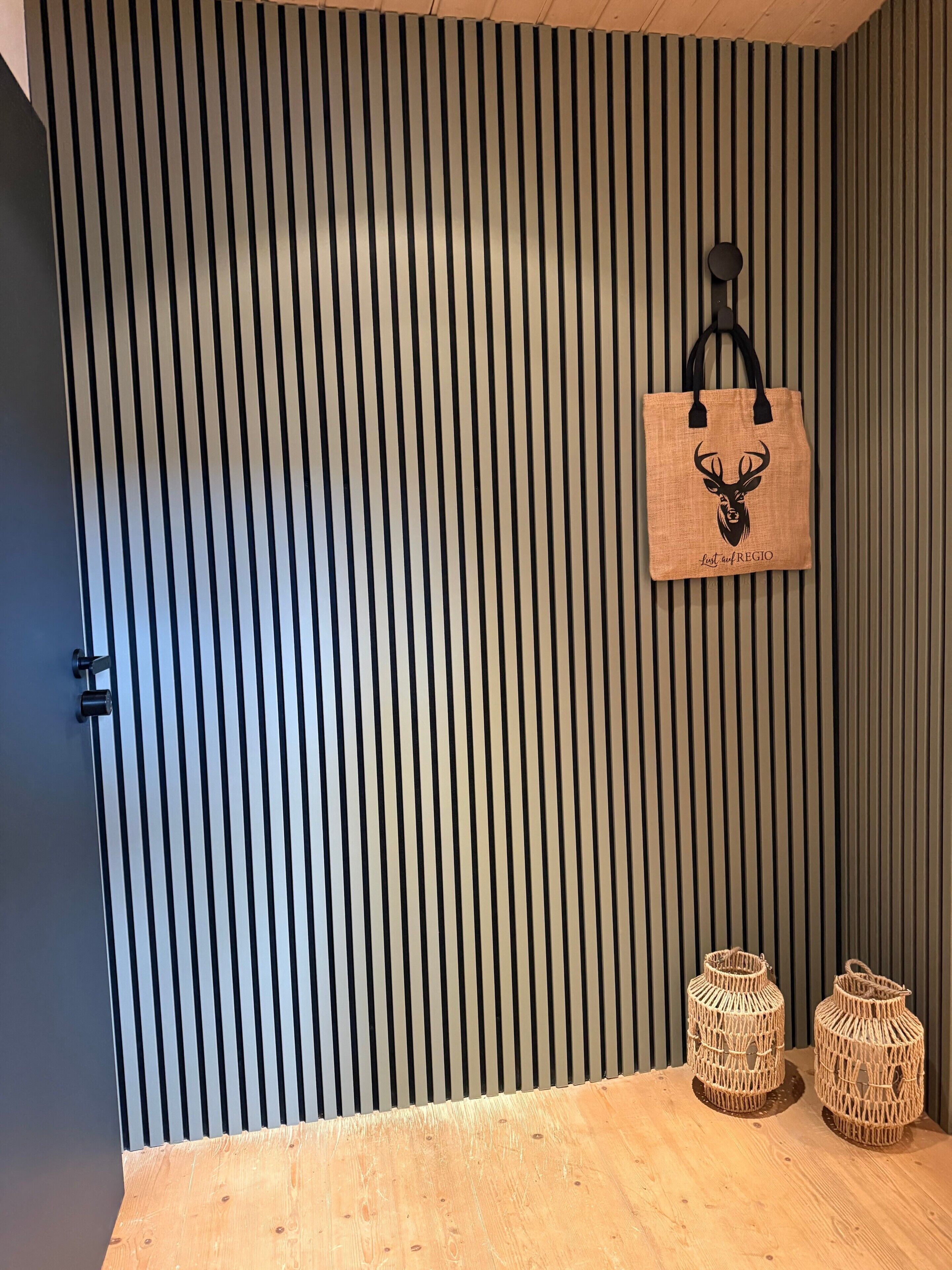 A room with a striped wall, a wooden floor, and a hanging bag with a deer head design.