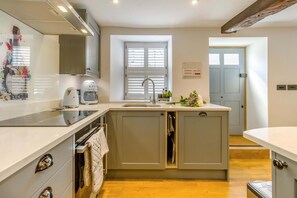 A modern kitchen with a central island, built-in appliances, and a window with blinds.