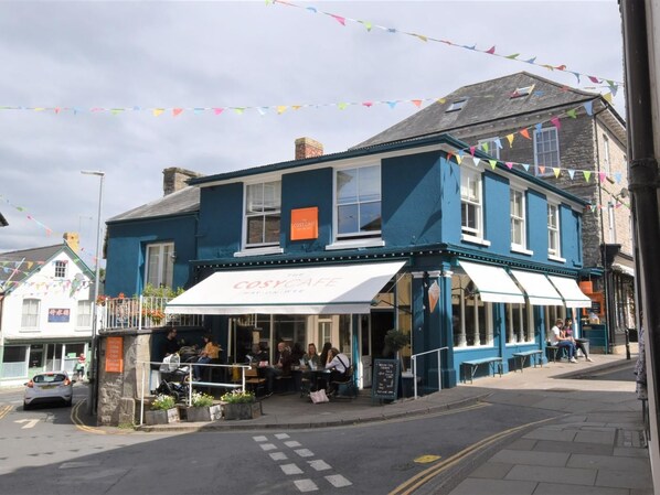 A corner building with a cafe named "The Cosy Cafe" and a sign for "The Cosy Cafe" on the facade.