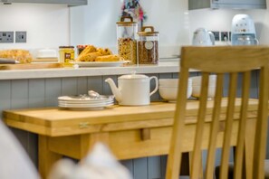 A kitchen with a wooden table, a white teapot, and jars of grains.