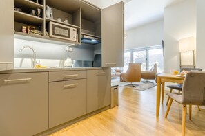 A modern kitchen with integrated appliances, a dining area with a table and chairs, and a view through the window.
