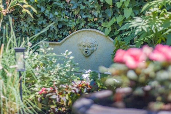 A garden with a stone headstone surrounded by greenery and flowers.