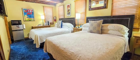 A hotel room with two beds, a refrigerator, a small table, and a ceiling fan.