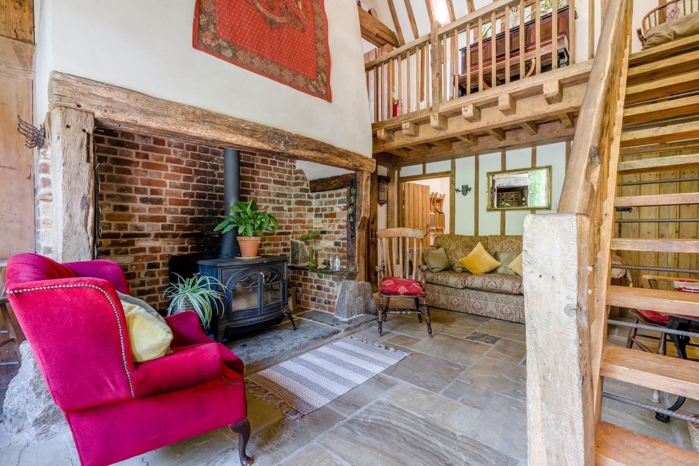 Un salon chaleureux avec une cheminée en briques, un fauteuil rouge et un escalier en bois.