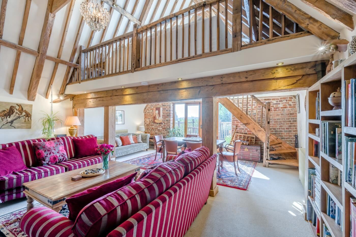 A spacious living area with a high ceiling, wooden beams, a staircase, and a fireplace.