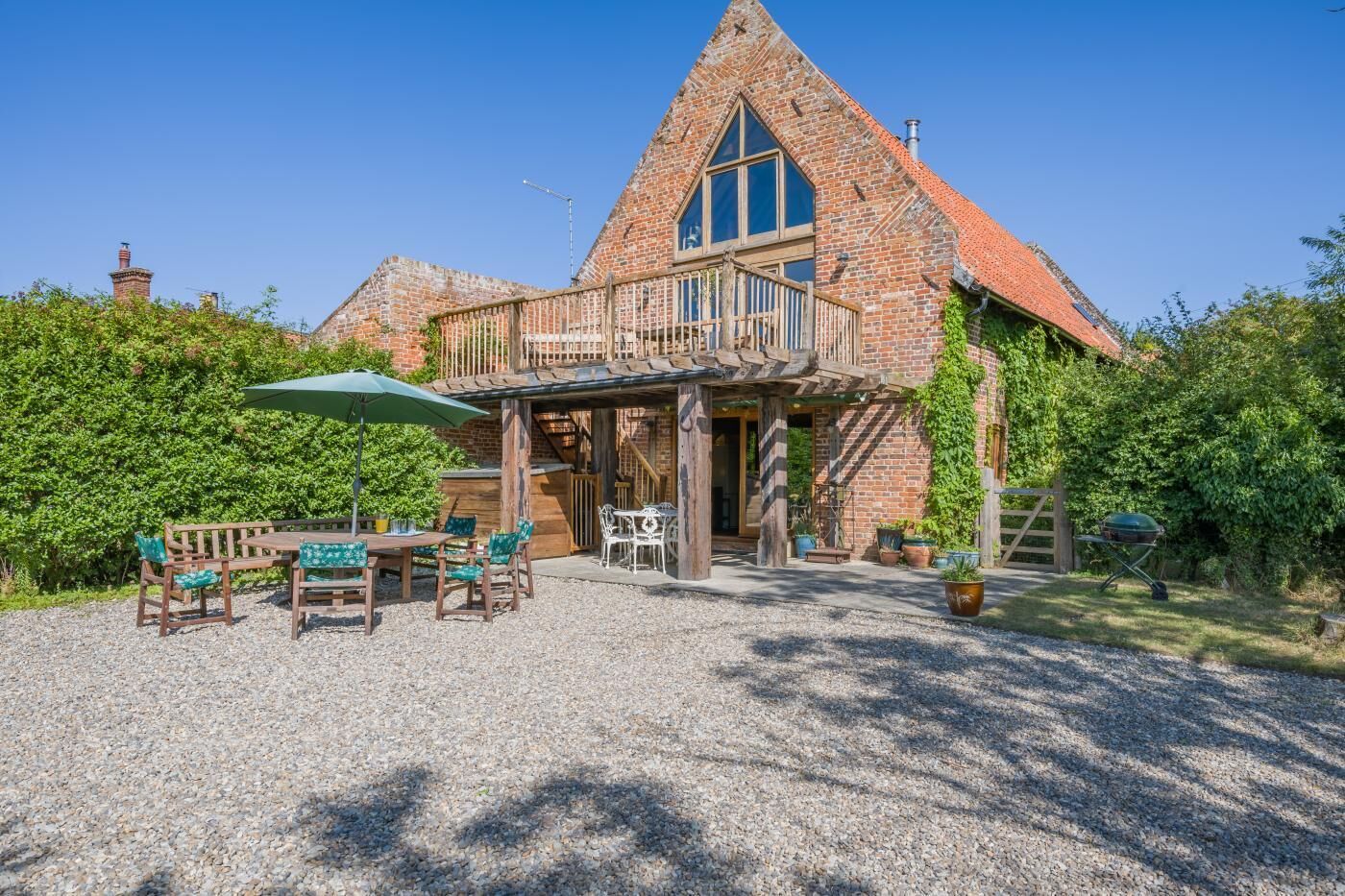A brick house with a large balcony, outdoor seating area, and a gravel driveway.