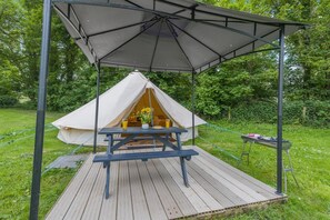 Ein Zelt mit Picknicktisch davor, umgeben von einer Holzterrasse und einer Überdachung.