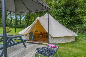 Ein Zelt mit einer überdachten Terrasse, einem Picknicktisch und Campingausrüstung.