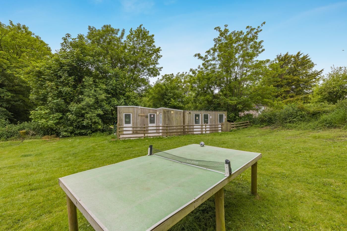 An outdoor ping pong table in a grassy area with a wooden structure in the background.