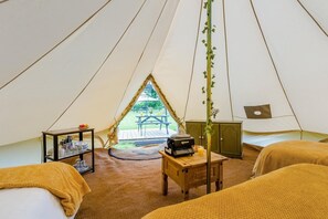 A tented accommodation with two beds, a table with a radio, and a view of an outdoor picnic area.