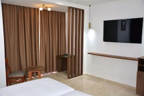 Habitación de hotel con cama, escritorio, silla, televisor y cortina divisoria.